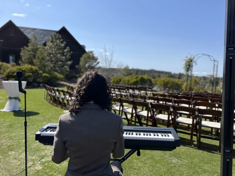 Gabe from behind, playing for rows of guests' chairs at a wedding ceremony